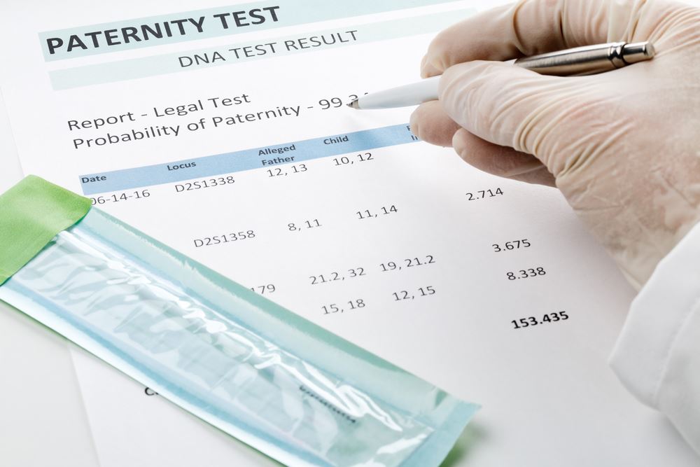 Gloved hand holding a pen above a paternity test.